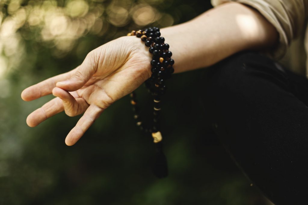 Braço de uma mulher, com pulseira de contas, sentada em posição de meditação.